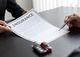 Person signing an insurance document; car keys and a toy car on the table.