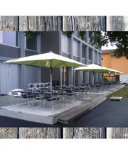 Außenbereich mit Tischen und Stühlen, überdacht von großen Sonnenschirmen vor einem Gebäude.