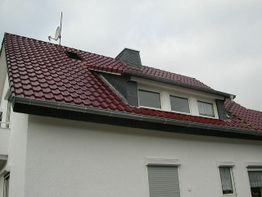 Dach mit roten Ziegeln und Dachfenster auf einem weißen Haus bei bewölktem Himmel.