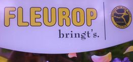 Fleurop-Logo mit Slogan "bringt's" und gelbem Emblem, umgeben von Blumen.