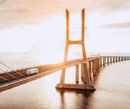 Puente sobre el agua iluminado por el sol al atardecer, con un camión cruzando.