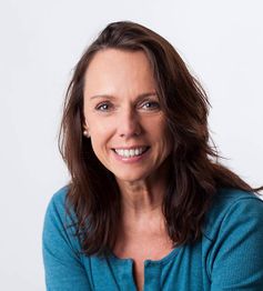 Eine lachende Frau mit dunkelbraunem Haar in einem blauen Oberteil vor weißem Hintergrund.