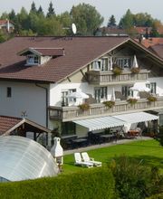 Großes Haus mit Balkon, grünem Garten und überdachtem Pool, umgeben von Bäumen und Gebäuden.