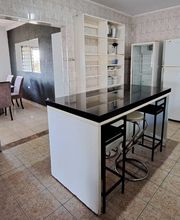 Cozinha com ilha central, cadeiras, geladeira, fogão e acesso à sala de jantar ao fundo.