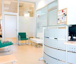 Sala de espera de oficina médica con sillas verdes y blancas, y un escritorio con computadora.