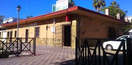 Edificio amarillo con techo rojo, puertas cerradas y un coche blanco aparcado al lado.