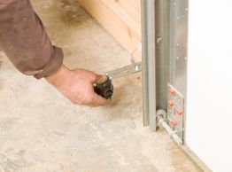 Person adjusting a garage door mechanism on a concrete floor.