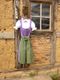 Dirndl in Lila und Grün hängt an einer Holzwand vor einem Fenster mit Glasbausteinen.
