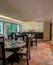 Restaurante elegante con mesas servidas, bar a la derecha y ventanas con vista a un jardín.