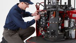 Técnico reparando la maquinaria interna de una carretilla elevadora roja con atención al detalle.