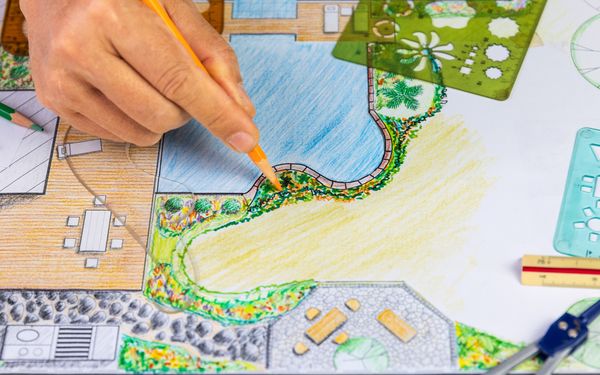 Landschaftsbauer zeichnet einen Plan für die zukünftige Parkgestaltung. Mit eingeplant ist unter anderem eine große Grünfläche, ein Sitzbereich in Form einer Terrasse, außerdem ein Teich.