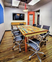 Modern conference room with a wooden table, black chairs, and a wall-mounted TV.