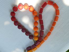 Rote und orangefarbene Perlenkette in Herzform auf weißem Hintergrund.