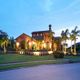 Modern villa with palm trees and warm lighting against a blue sky backdrop at dusk.