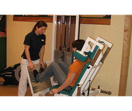 Eine Trainerin hilft einer Person bei der Beinpresse im Fitnessstudio.
