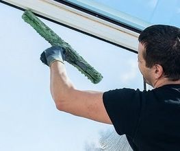 Person reinigt ein Fenster mit einem Schwamm; Text über Gebäudewartung in der Region Luzern.