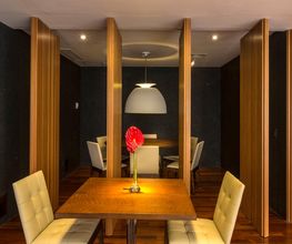 Sala de jantar moderna com madeira, cadeiras brancas e luminária central acima da mesa.