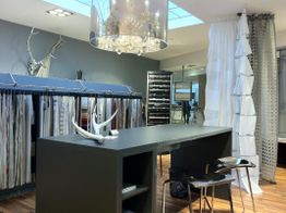 Moderner Raum mit Stoffmustern, langer Theke, Kronleuchter und weißen Vorhängen.