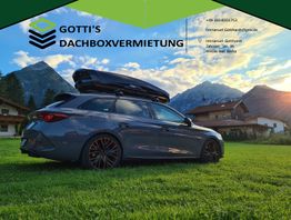 Auto mit Dachbox vor Bergen, Werbeinfo von Gotti's Dachboxvermietung oben rechts.