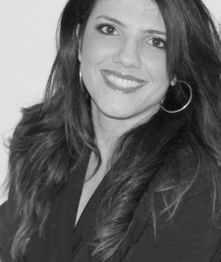 Mulher sorrindo em foto em preto e branco, com cabelos longos e brincos de argola.