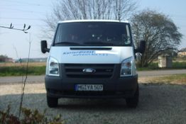 Ein weißer Lieferwagen mit der Aufschrift "Kurierdienst" parkt vor einer ländlichen Straße.