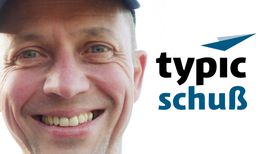 Lächelnder Mann mit Mütze neben dem Wort "typic schuß" und einem blauen Logo.