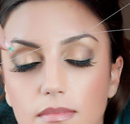 Woman getting eyebrows threaded, eyes closed, with focus on threading technique.