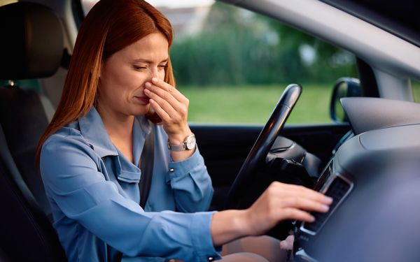 Eine Frau in einem Auto hält sich ihre Nase zu, nachdem sie die Klimaanlage angeschaltet hat.