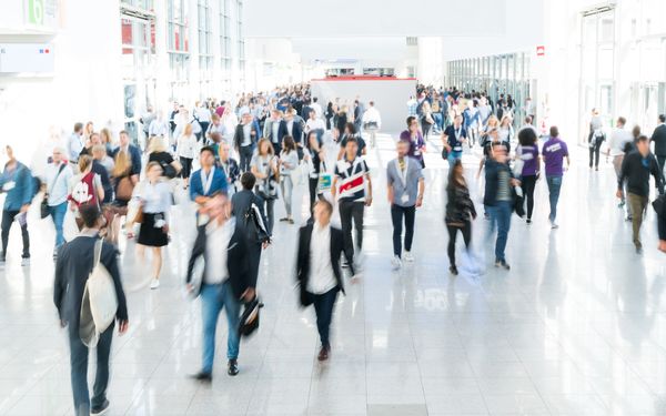 Eine Vielzahl an Menschen bewegen sich auf einem Messegelände fort.