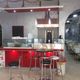 Interno di un ristorante con bancone rosso e tavoli bianchi, arredamento moderno.