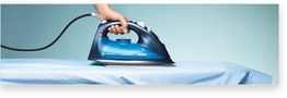 Hand bügelt Hemd mit elektrischem Bügeleisen auf einem Bügelbrett vor blauem Hintergrund.