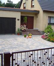 Einfamilienhaus mit Garage, gepflegtem Garten und Pflastersteinen im Hof, geschlossene Tor.