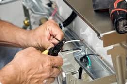 Hands using pliers to work on appliance wiring, with tools visible in the background.