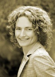 Person mit lockigem Haar lächelt in die Kamera, trägt kariertes Hemd. Sepia-Tonfoto.