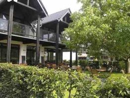 Modernes Gebäude mit Glasbalkonen und Terrasse, umgeben von Bäumen und Hecken im Garten.