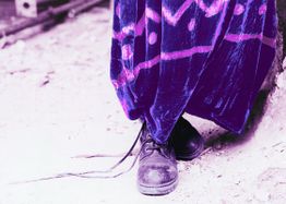 Lila Kleid und schwarze Stiefel auf staubigem Boden, hervorstehende Schnürsenkel.