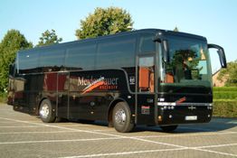 Schwarzer Reisebus auf einem Parkplatz bei Tageslicht, umgeben von Bäumen und Gebäuden.