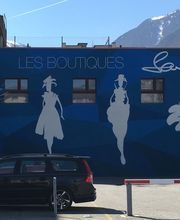 Wand mit stilisierten Modefiguren und Auto im Vordergrund, umgeben von Bergen, "Les Boutiques".