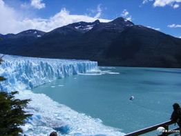 Geleira imponente ao lado de um lago azul com montanhas ao fundo.