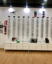 Tienda de óptica con expositores de gafas vacíos y muebles blancos sobre piso de madera.