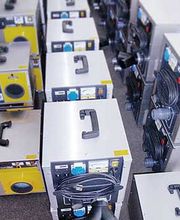 Mehrere industrielle Geräte mit Tragegriffen und Kabeln, dicht nebeneinander auf dem Boden platziert.