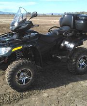 Cuatrimoto negra aparcada en terreno arenoso, fondo de paisaje con montañas distantes.
