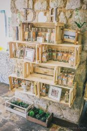 Caixotes de madeira na parede com garrafas, molduras e plantas em um ambiente rústico.