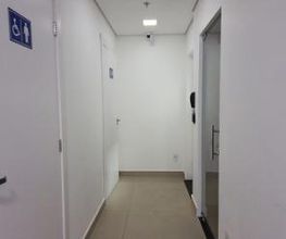 Corredor com portas brancas e placa indicando banheiro acessível à esquerda.