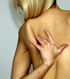 Eine Person mit blondem Haar kratzt sich den Rücken.