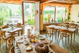 Gemütliches Café mit gedeckten Holztischen, großen Fenstern und Blick auf einen Garten.