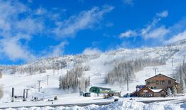 Snowy ski resort with chairlifts and lodge under a bright blue sky.