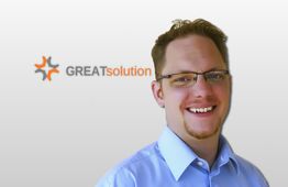 Ein lächelnder Mann mit Brille vor einem Firmenlogo mit dem Text "GREATSolution".