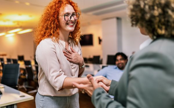 Zwei Kolleginnen begrüßen sich per Handschlag im Büro und stimmen sich zur Urlaubsvertretung ab.