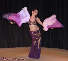 Eine Tänzerin mit Schleiern in violettem Kostüm vor schwarzem Hintergrund.